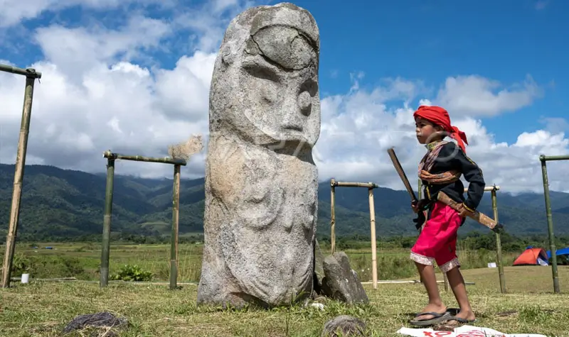 Seorang anak mengenakan pakaian adat melintas di depan patung Tadulako di situs Cagar Budaya Tadulako di Desa Bariri, Lore Tengah, Poso, Sulawesi Tengah, Jumat (16/6/2023). (ANTARA FOTO/basri marzuki)